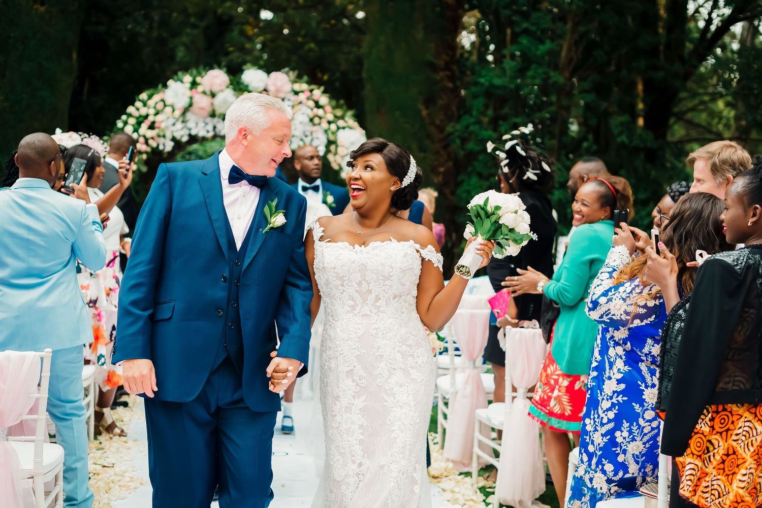 Wedding guests celebrate by blowing bubbles during an outdoor garden ceremony.