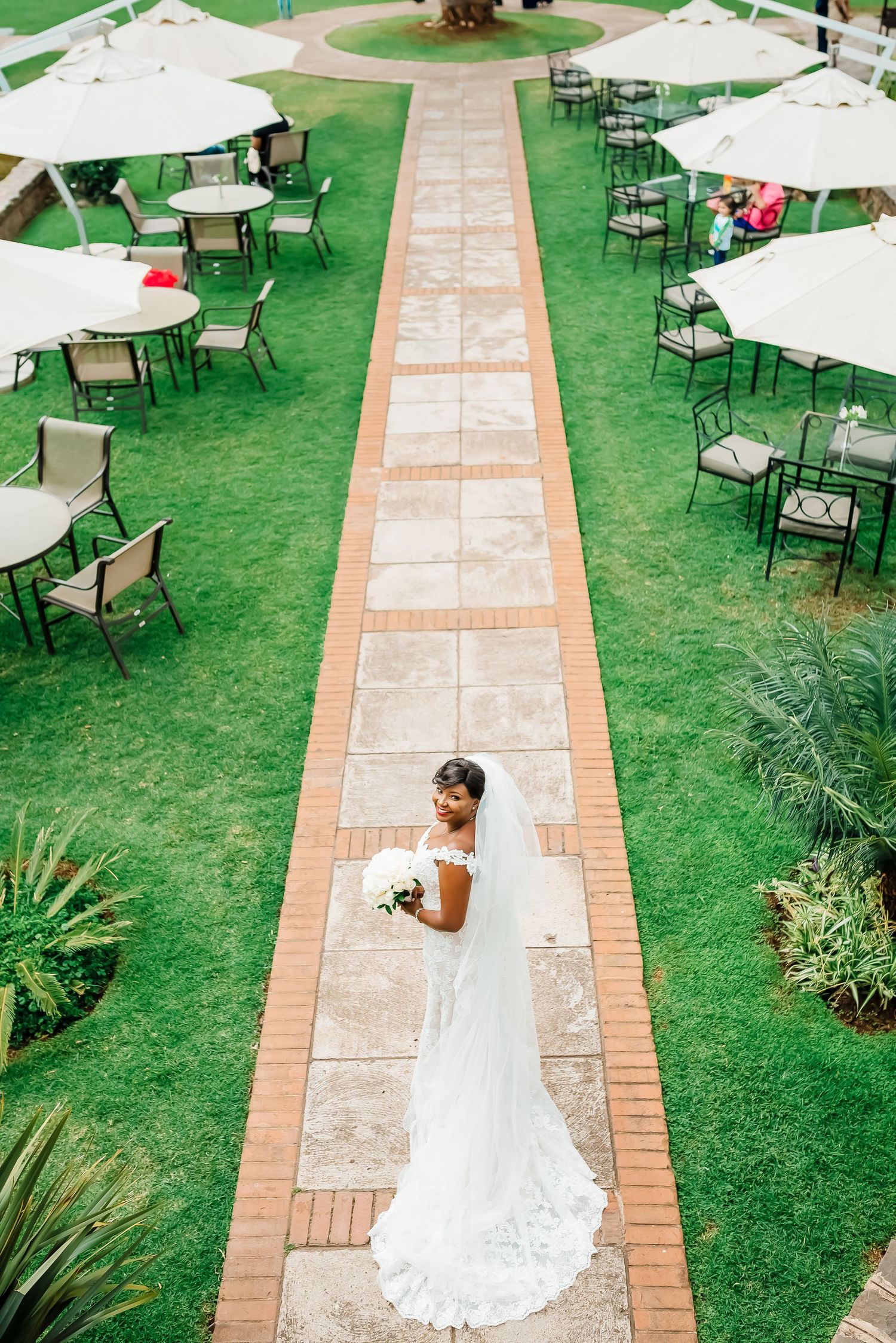 Aerial view of an elegant outdoor wedding reception setup with white umbrellas and tables on a manicured green lawn.