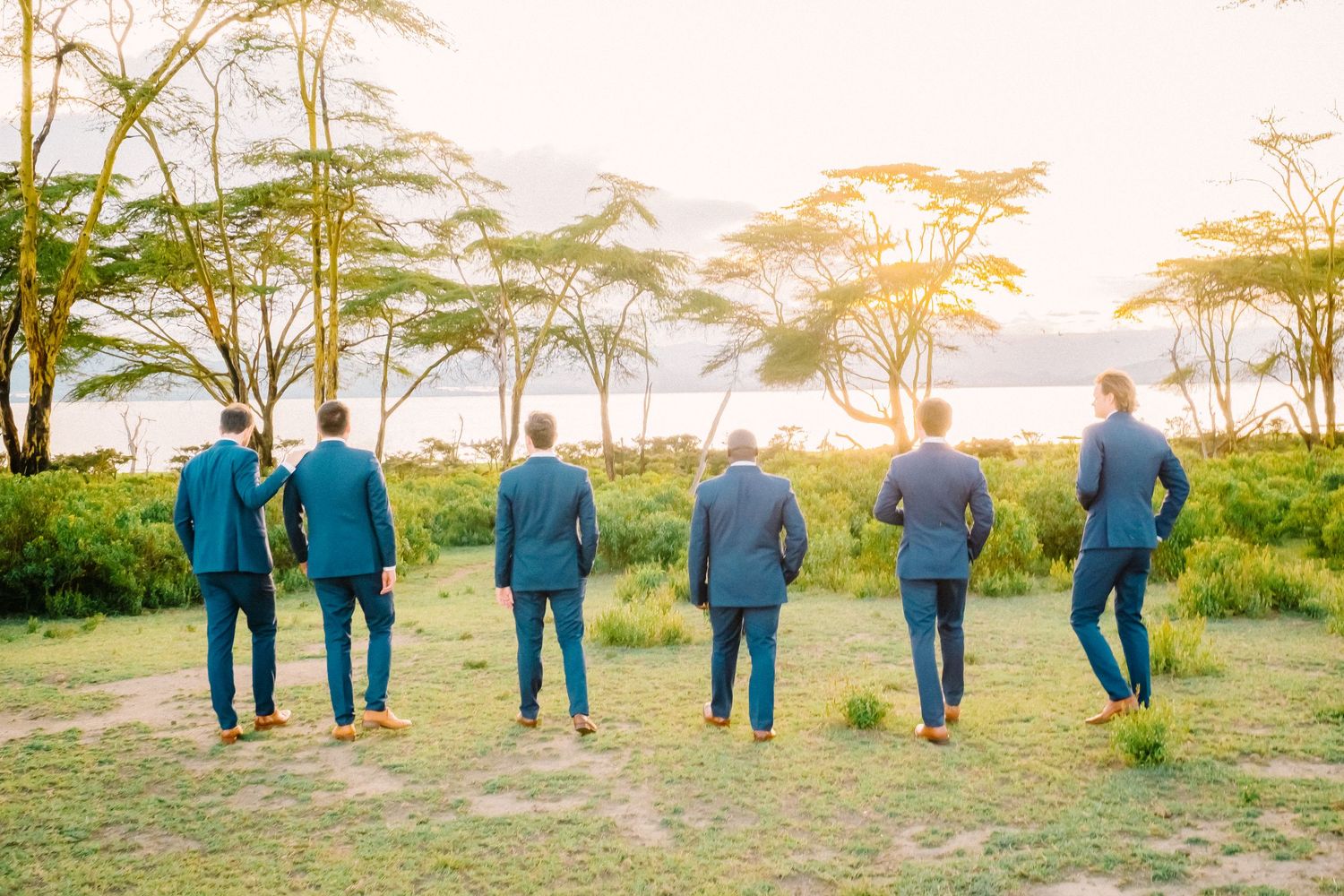 People in blue outfits stand together against a scenic African savanna landscape at sunset.
