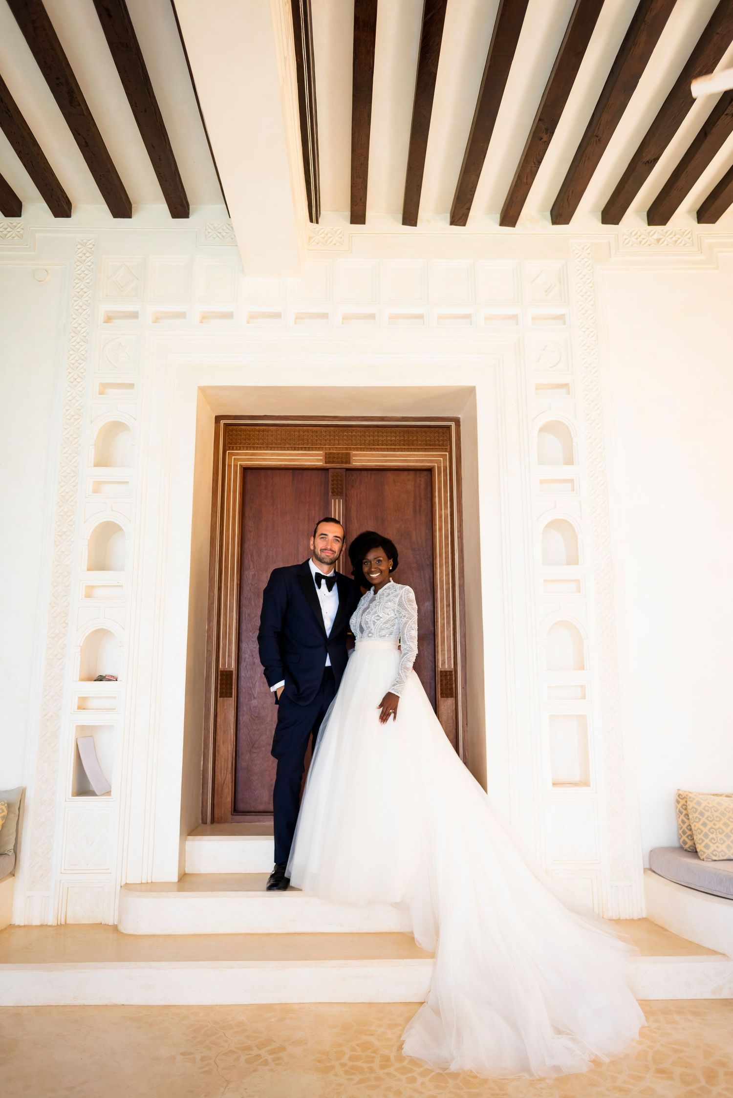 A wedding photo sequence showing a couple walking through an elegant white hallway with architectural arches and columns.