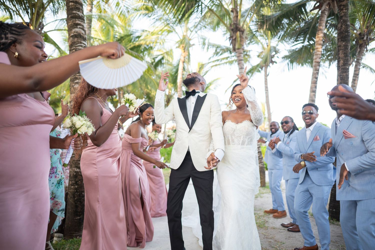 Wedding party celebrates with champagne toasts outdoors under palm trees at tropical destination ceremony.