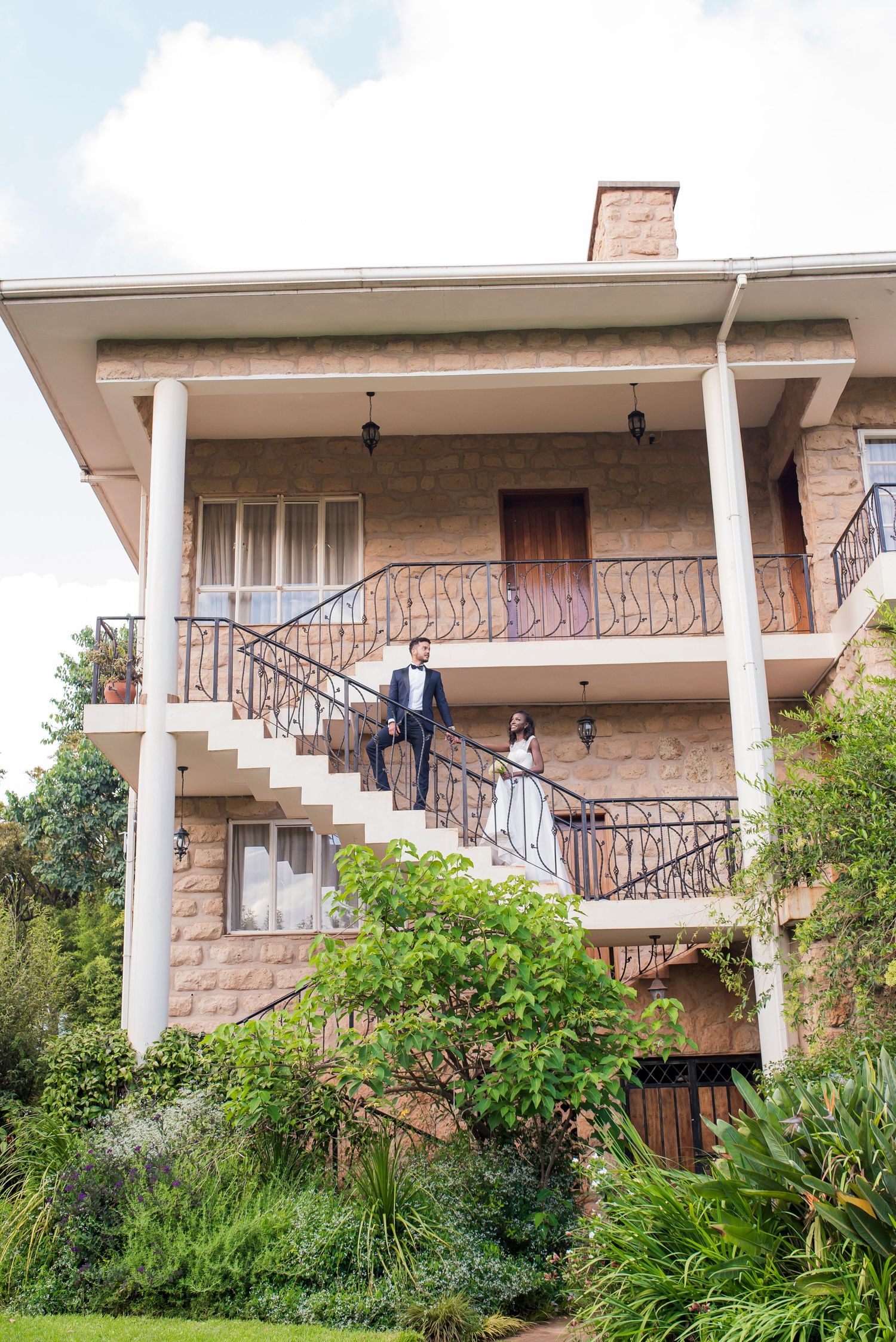 A modern two-story house with stone facade, white columns, and wrought iron railings on the balcony and stairs.