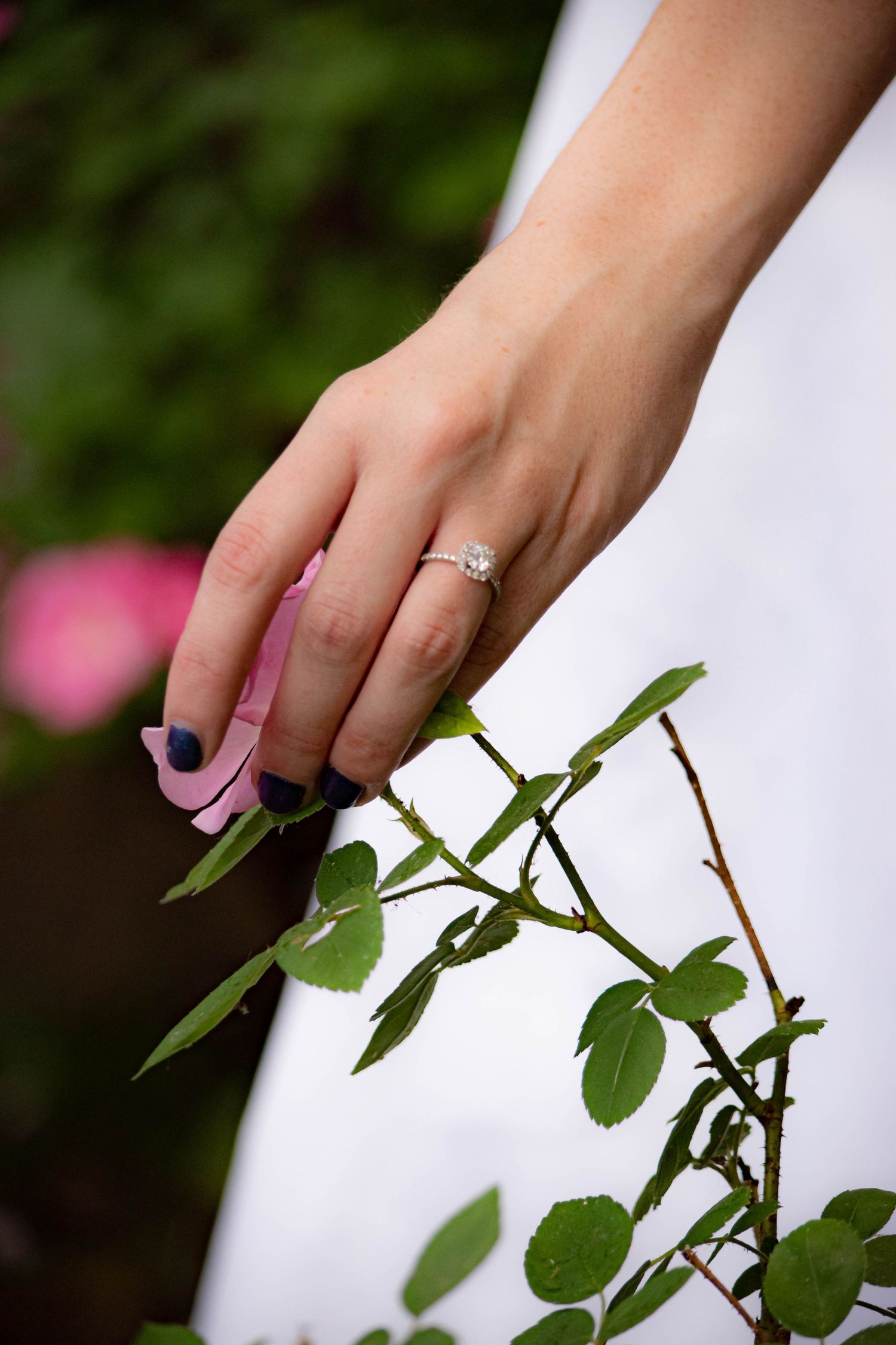 Close-up of hand with engagement ring touching green plant leaves against blurred background.