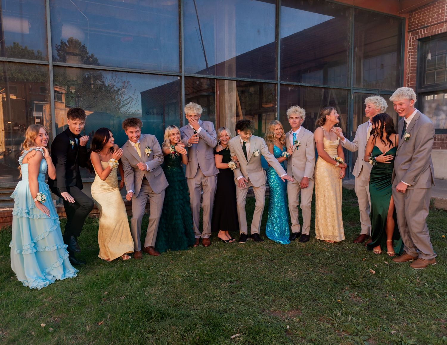 Group of teenagers in formal prom attire posing together outdoors at dusk, wearing elegant gowns and suits.