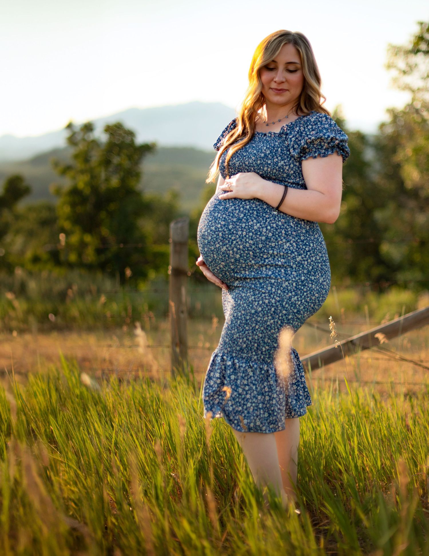 Maternity portraits in a blue floral dress taken in a sun-lit meadow.