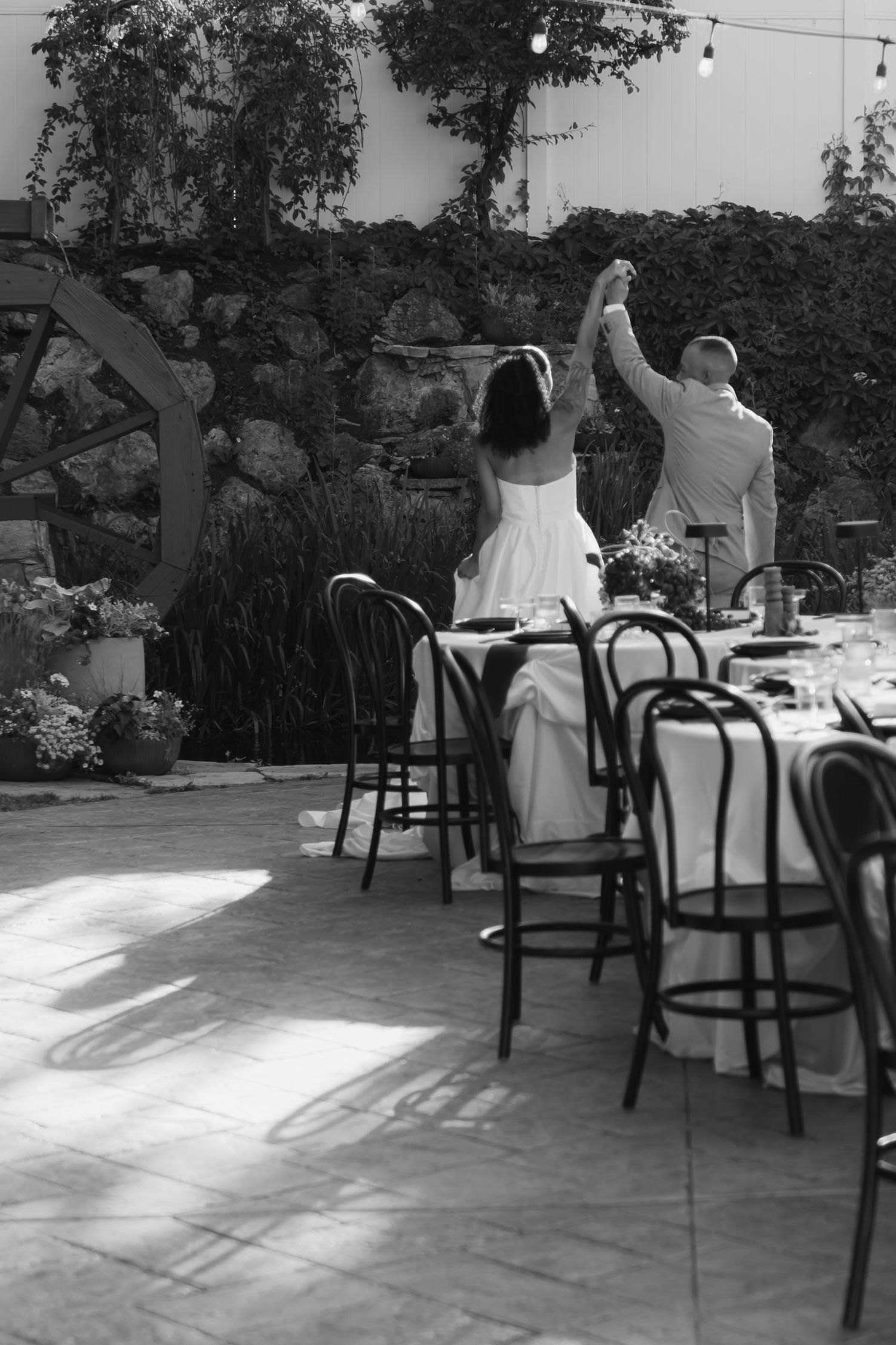 A black and white wedding scene with dancing figures in an outdoor garden setting.