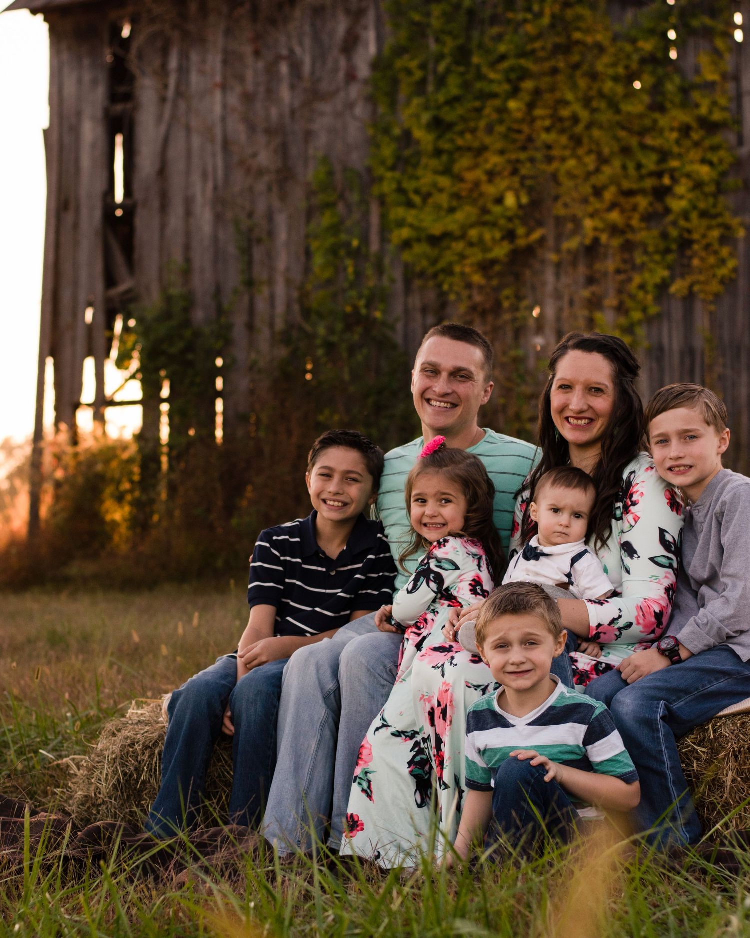 Family group portrait sitting together outdoors at sunset with rustic wooden fence background.