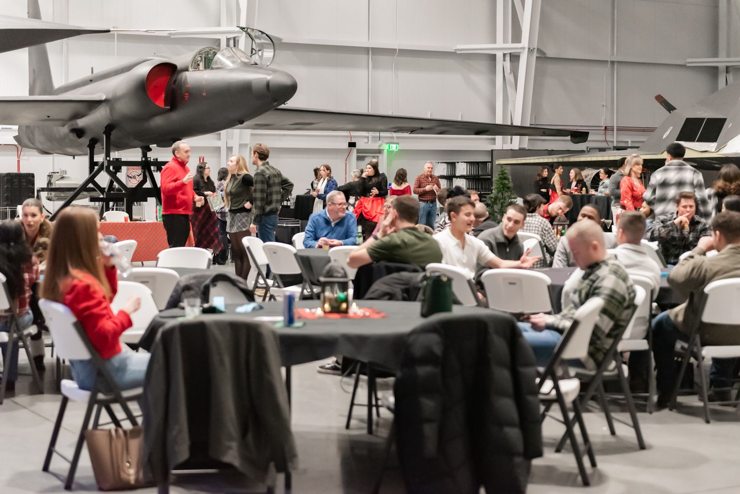 Large group dining event in aircraft hangar with planes on display.