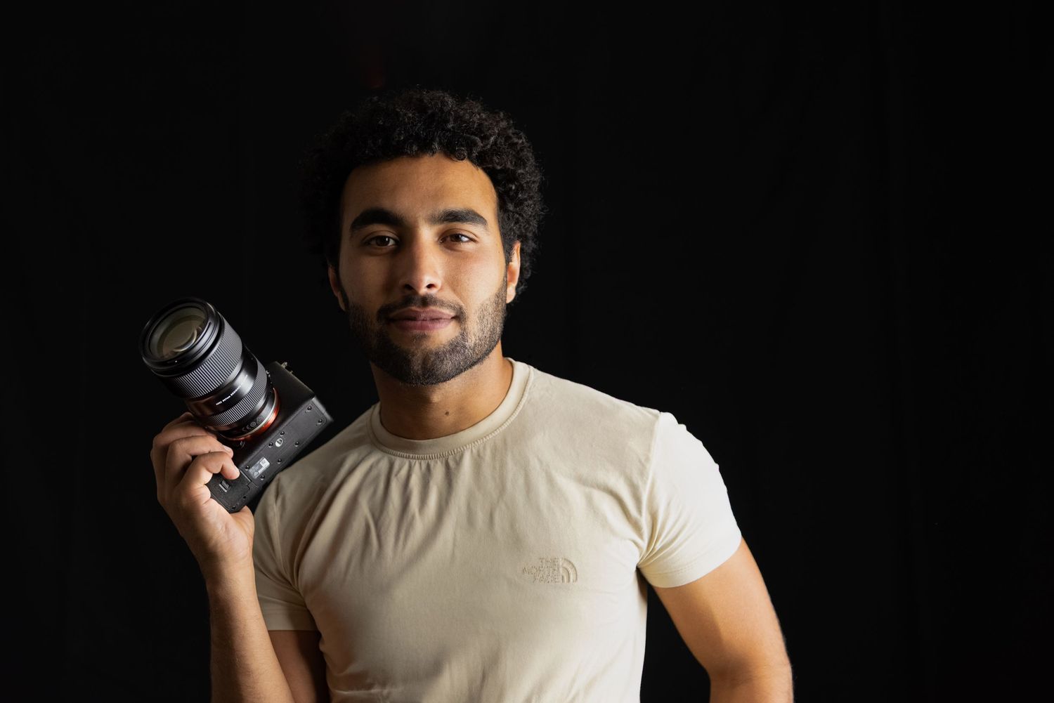 Portrait of photographer holding camera against dark background.