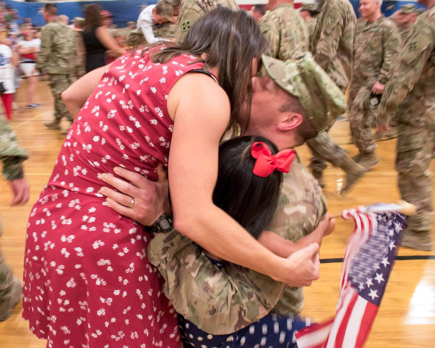 Military homecoming reunion with American flag and emotional embraces in gymnasium.