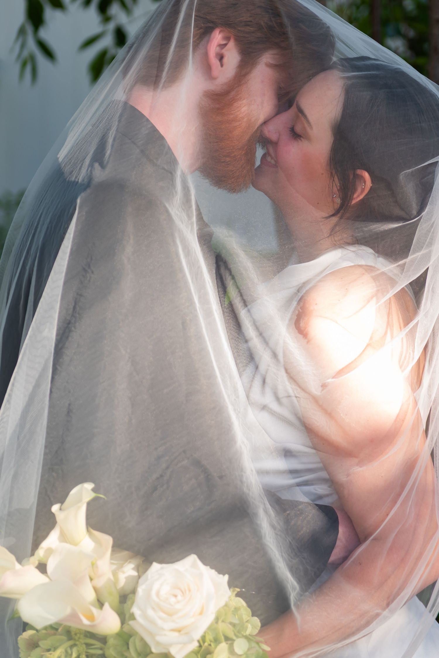 A romantic moment captured under a wedding veil with white roses in the foreground.