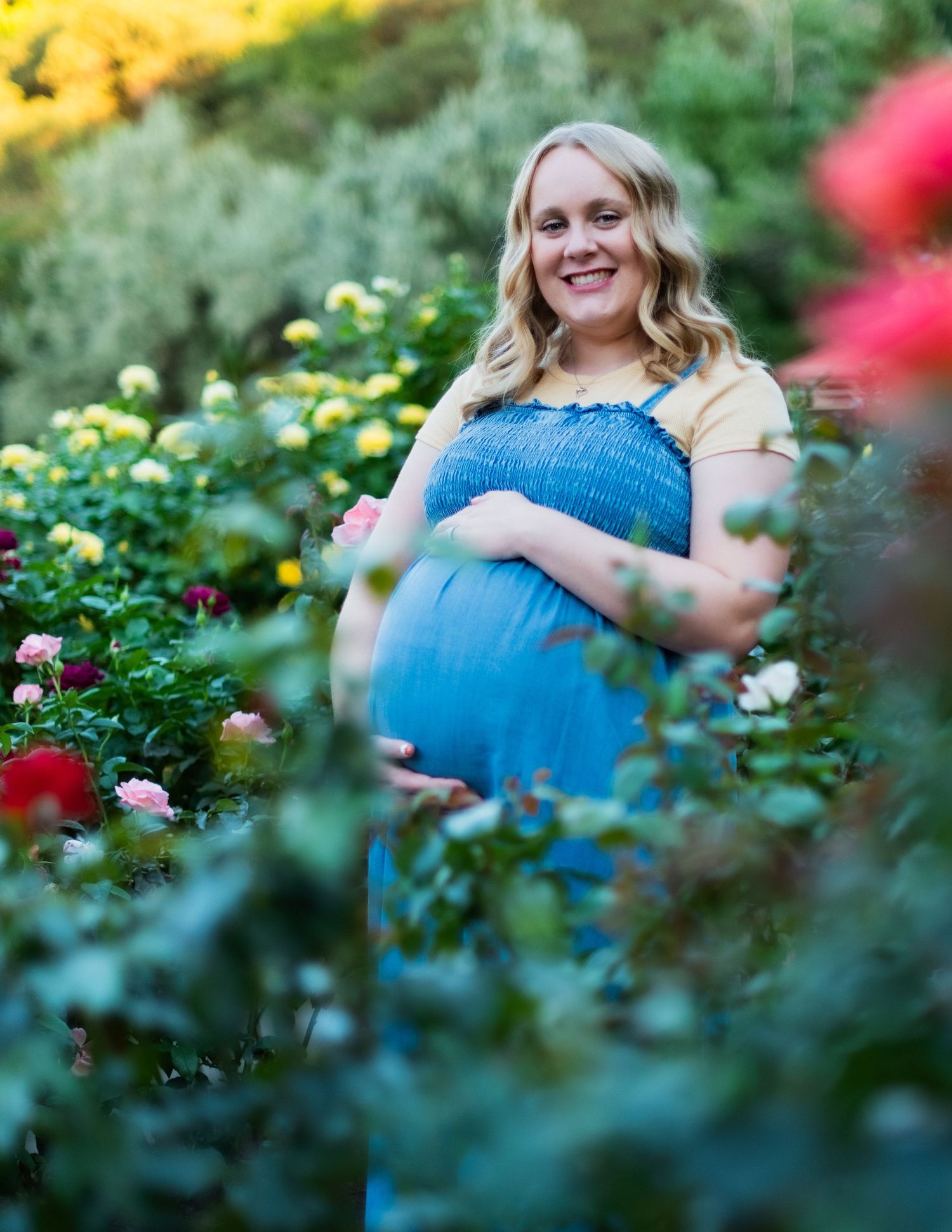 Maternity photos taken in a garden with vibrant yellow flowers and greenery in the background.