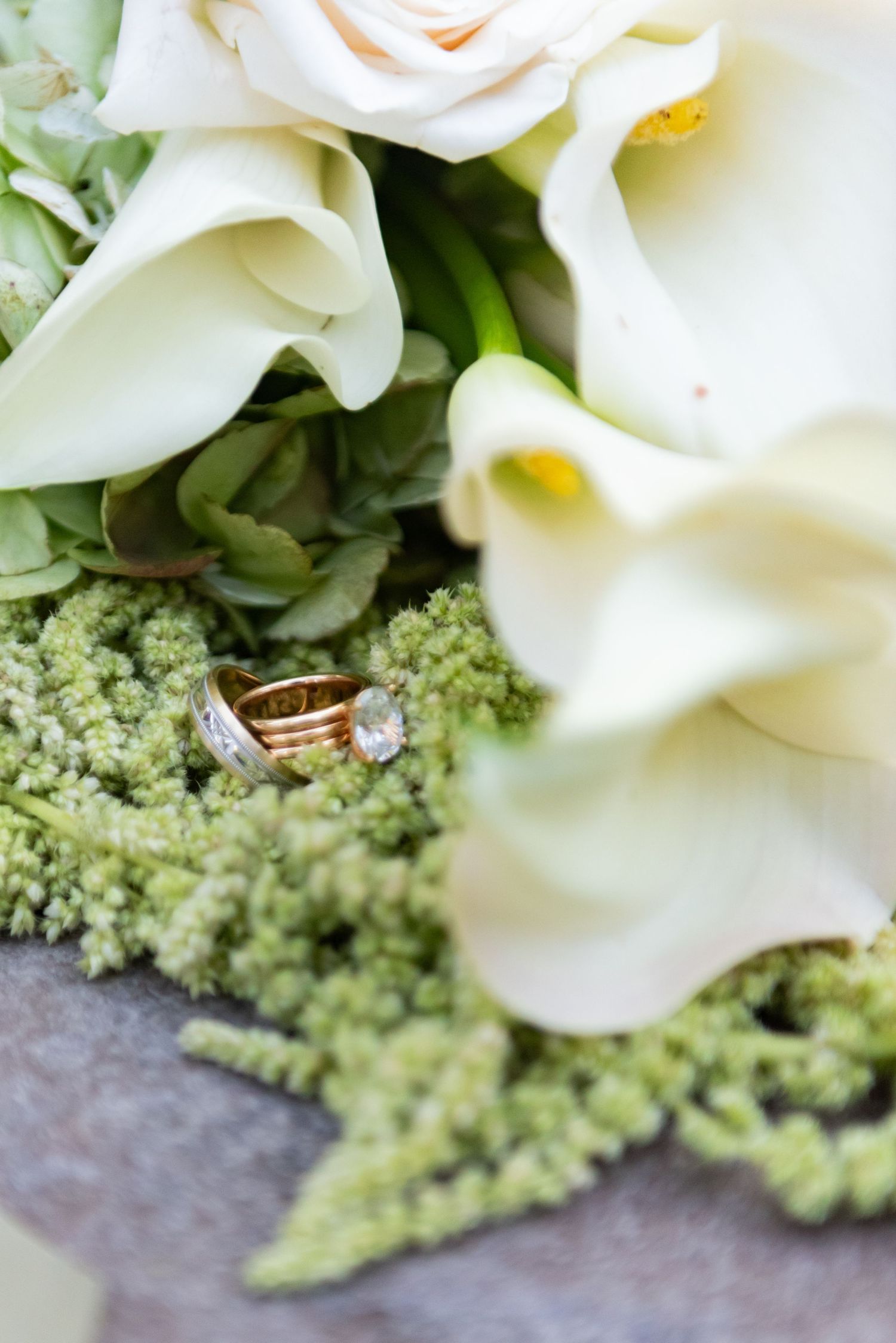 Wedding rings nestled among white calla lilies and delicate green floral arrangements.