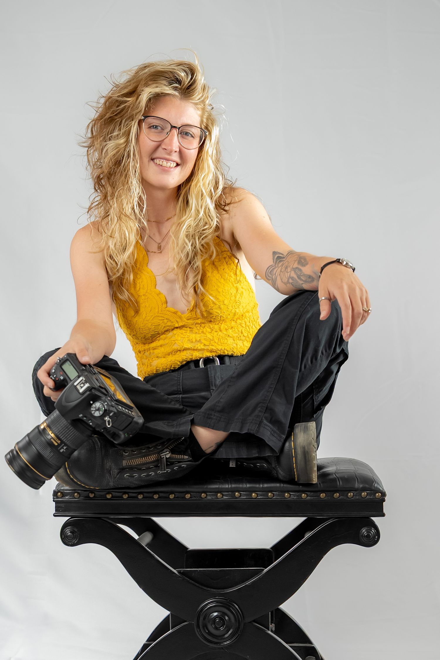 Professional photographer in yellow top poses with camera on black equipment.