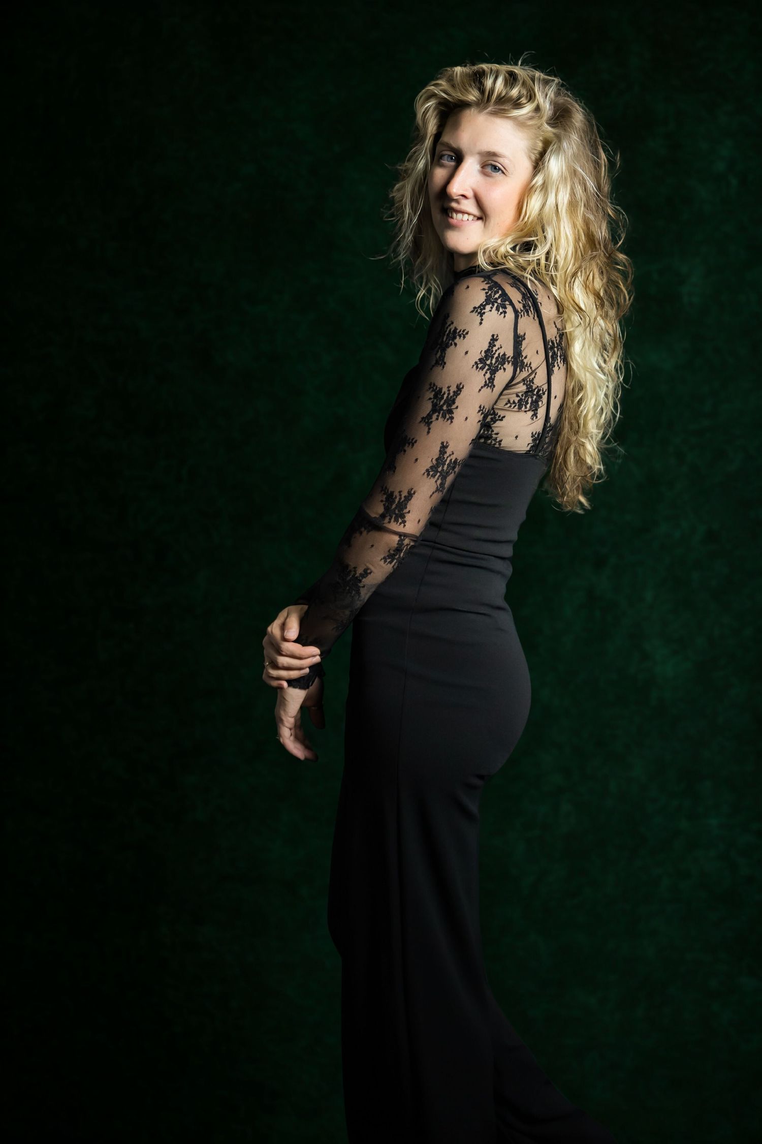 Elegant black evening dress with lace sleeves shown against dark green backdrop.
