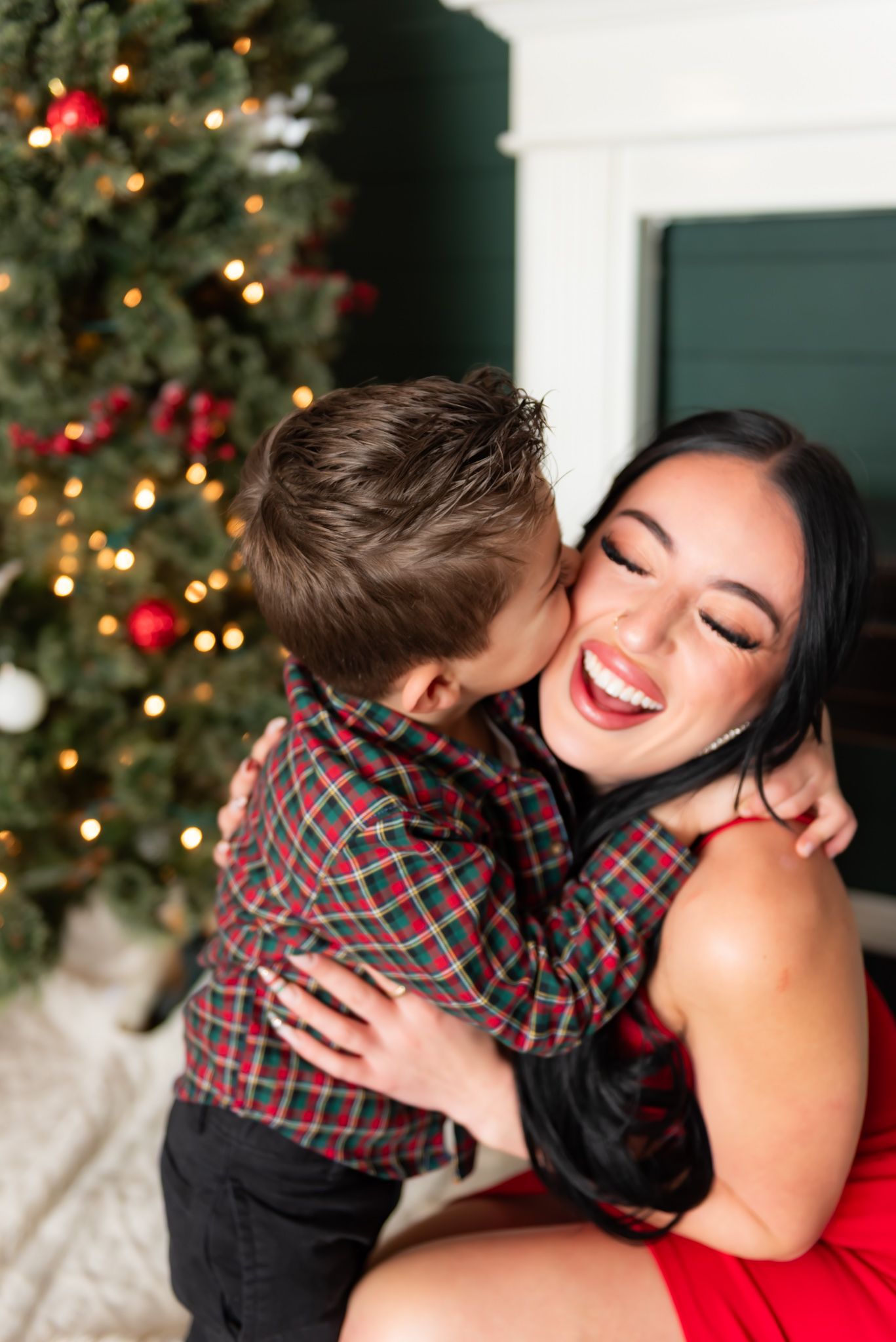 A joyful holiday moment shared between a child and woman in front of a decorated Christmas tree.