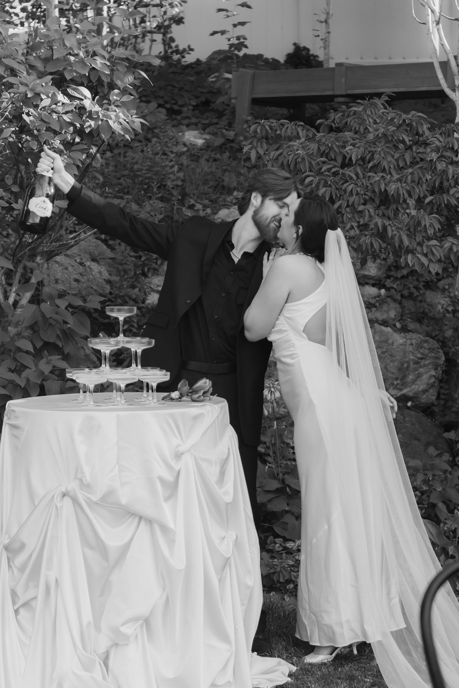 A black and white wedding photo of a couple sharing a moment by their champagne tower.