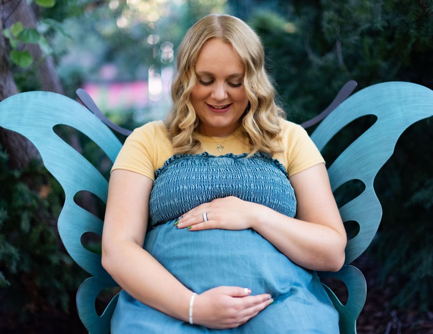 A blue maternity dress is showcased against a natural outdoor backdrop.
