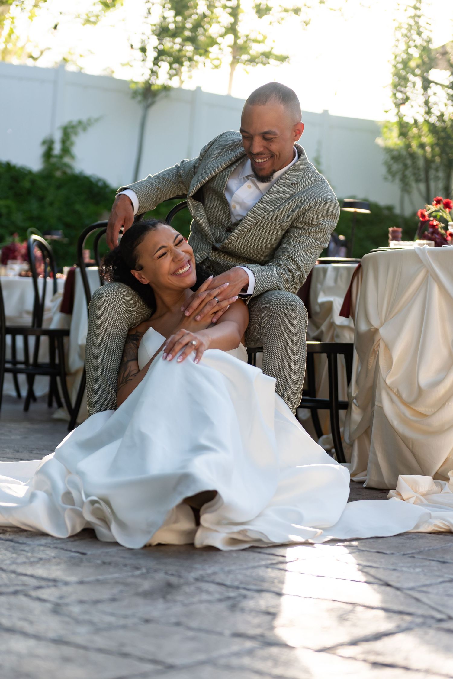 Romantic wedding couple in white dress and gray suit reclining on outdoor patio.