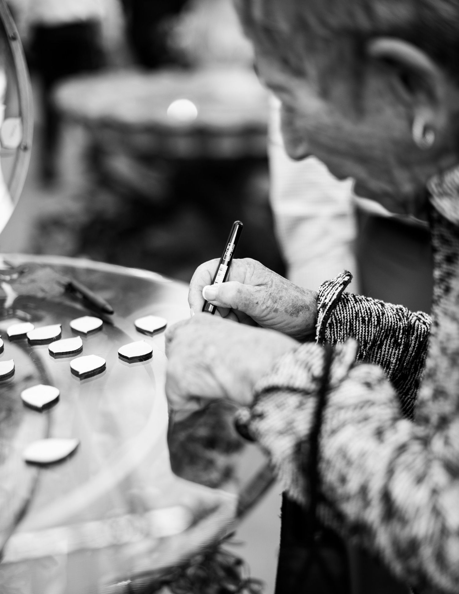 Elderly signing carefully on small wooden hearts on a glass table in black and white photography.