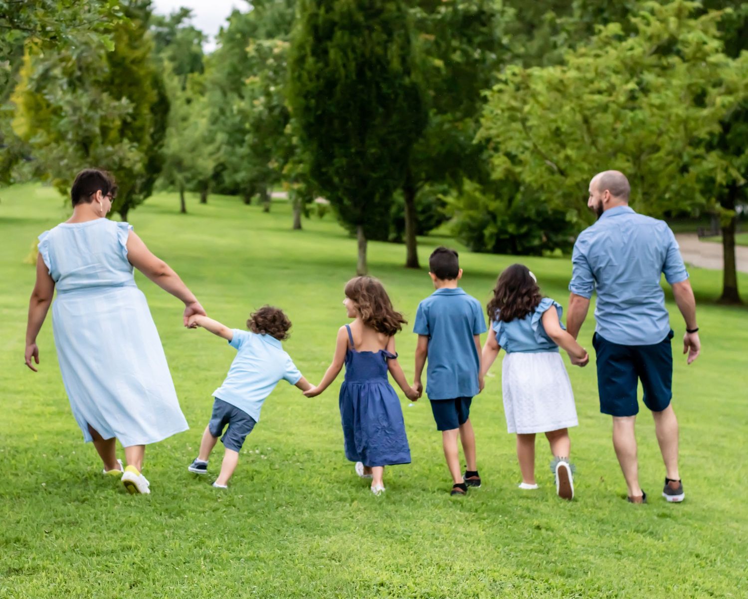 A group wearing coordinating blue and white outfits walks together on a grassy hill during a summer photoshoot.