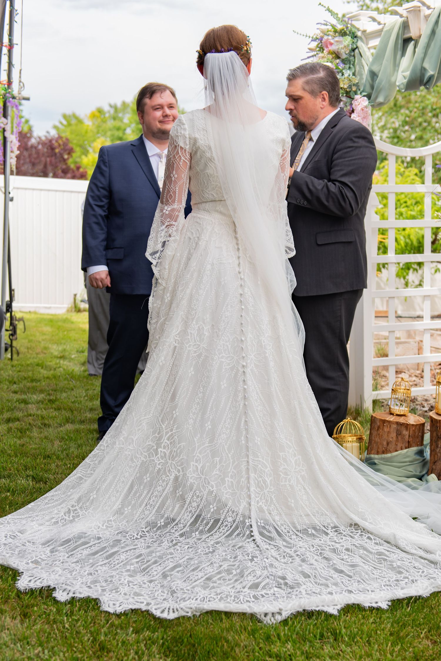 An elegant white wedding dress with a long lace train displayed outdoors.
