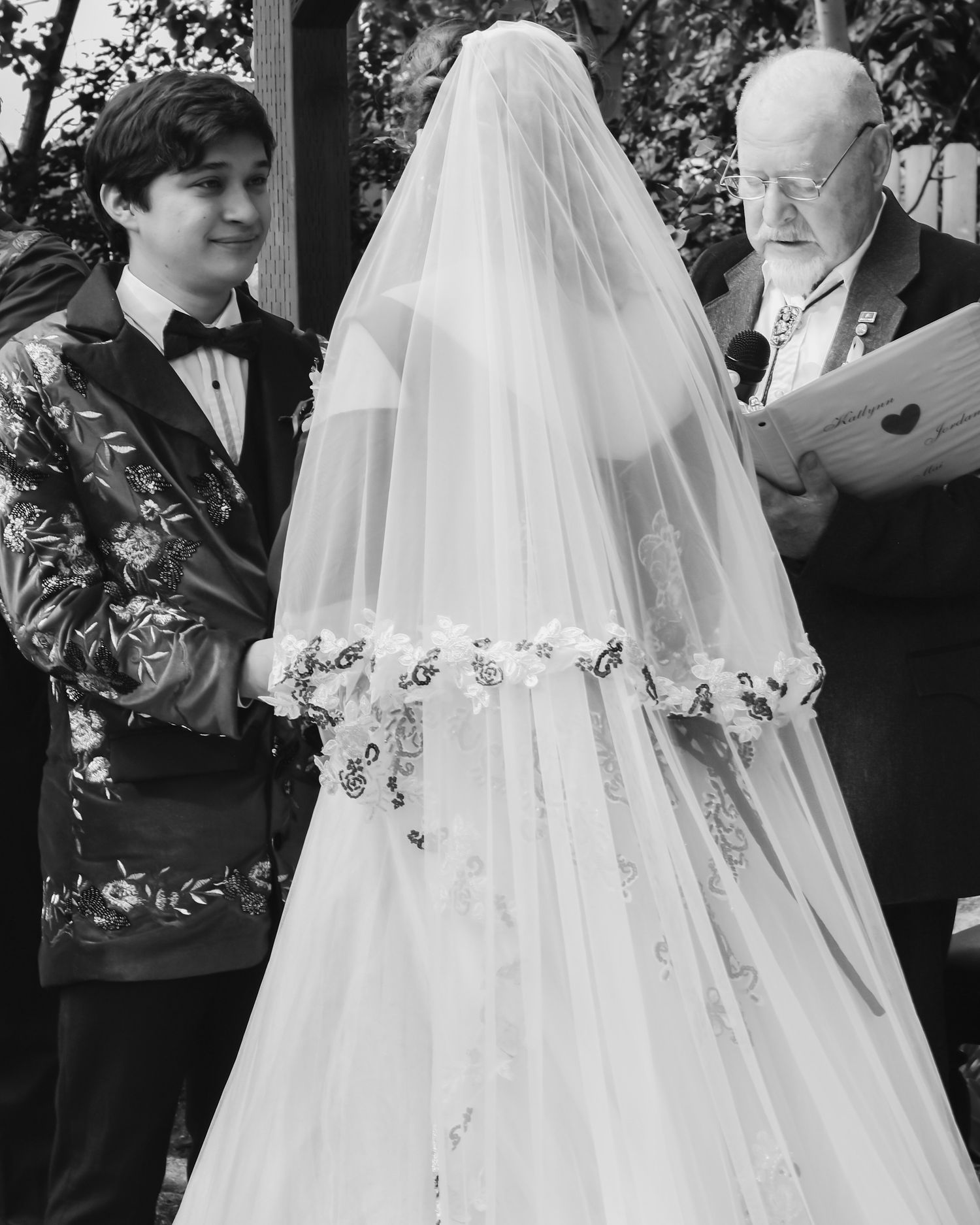 Black and white wedding ceremony photo with bride in detailed veil and officiant.