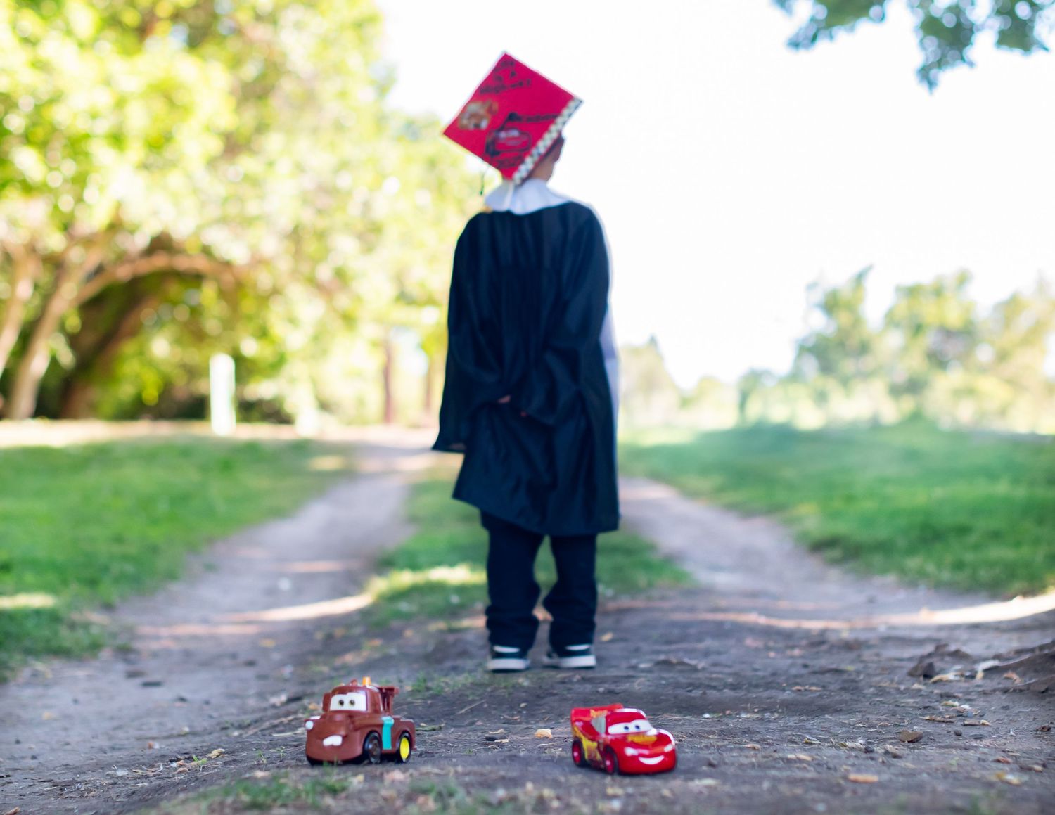 Creative graduation photo with cap floating above toy cars on path.