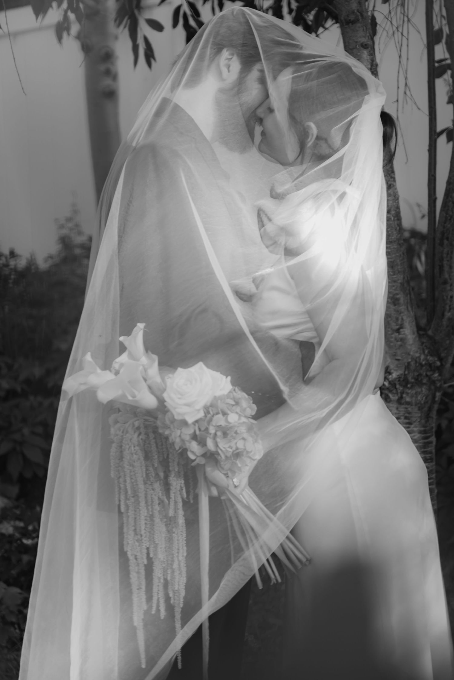 Ethereal bridal portraits with flowing white veil and bouquet in soft black and white.