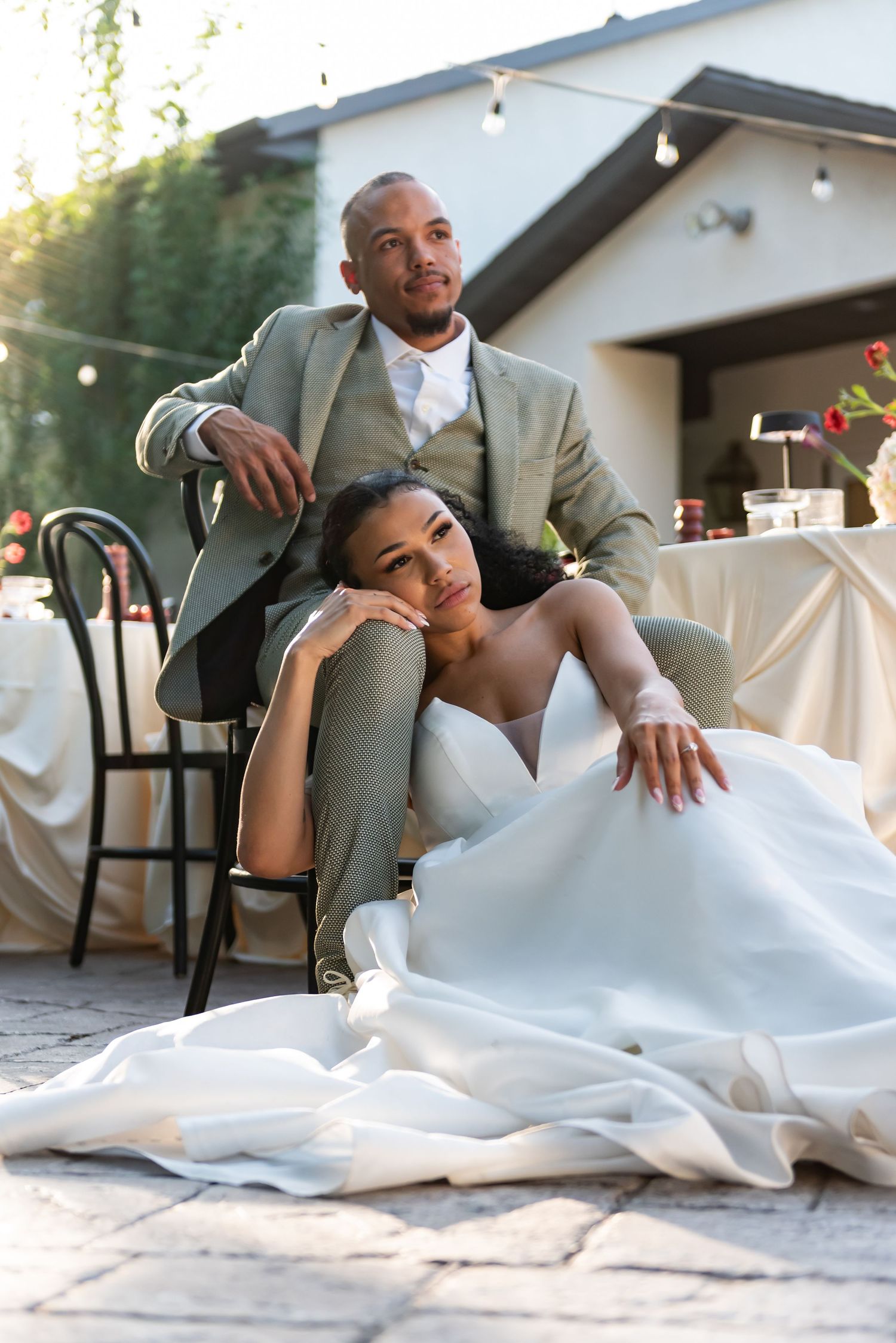 A relaxed wedding couple poses together on their reception patio.