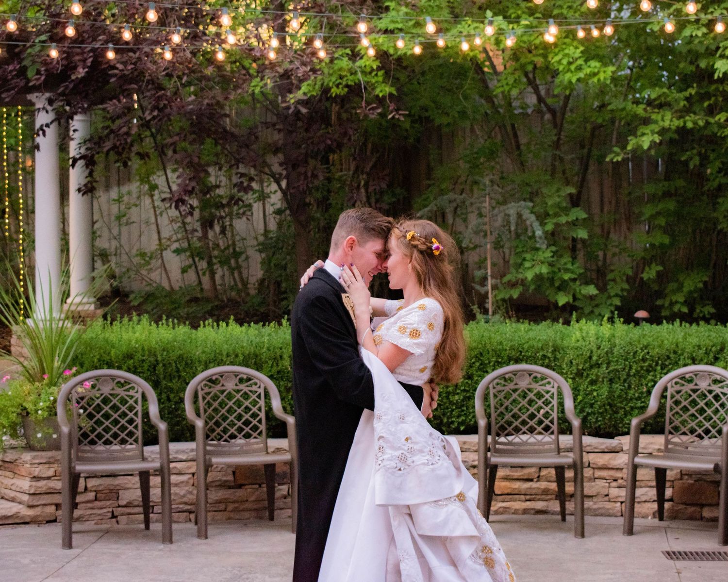 String lights illuminate an outdoor wedding venue as a couple shares a romantic moment.