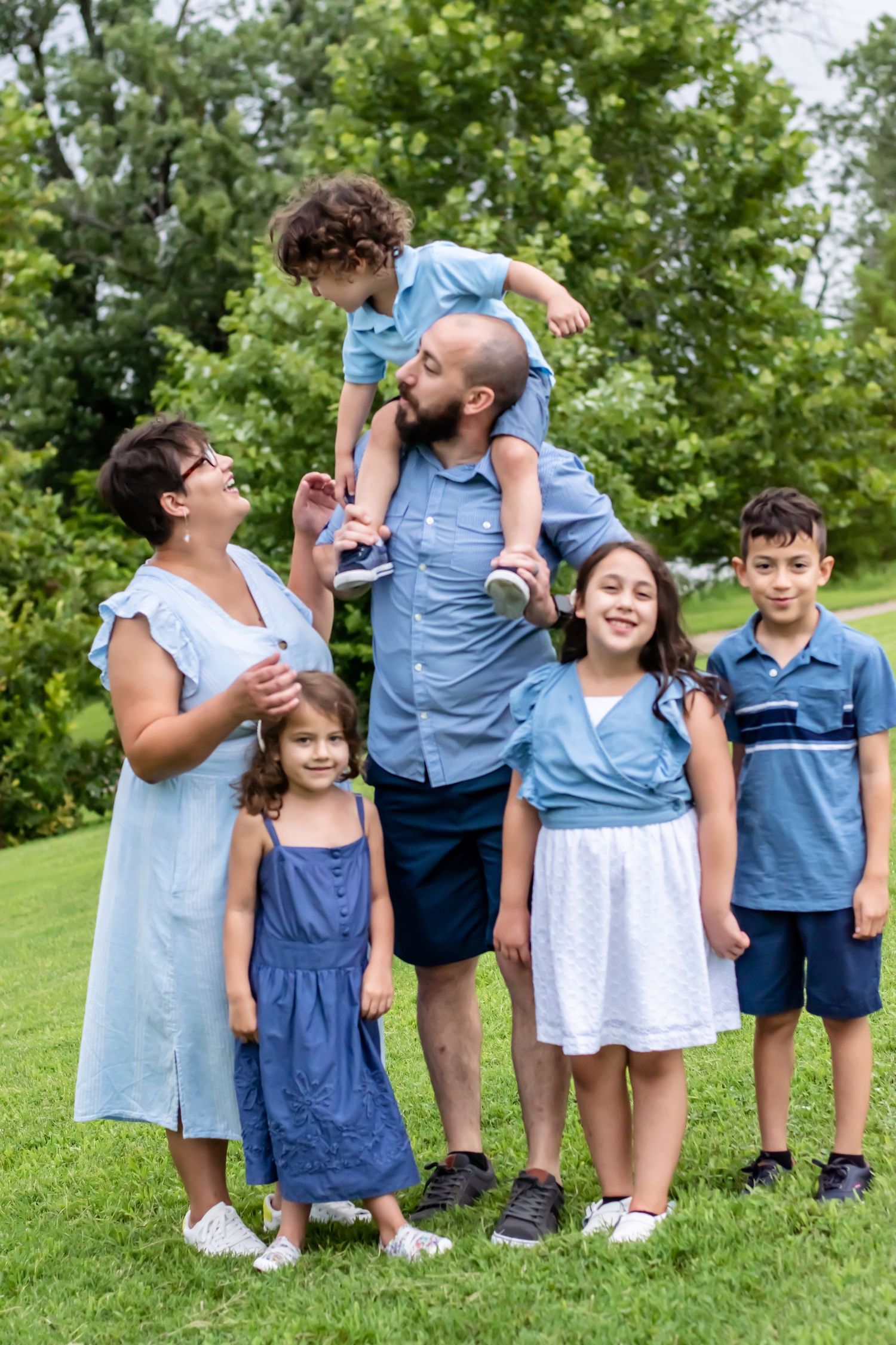 Family members in coordinating blue outfits pose playfully together on a green hillside.