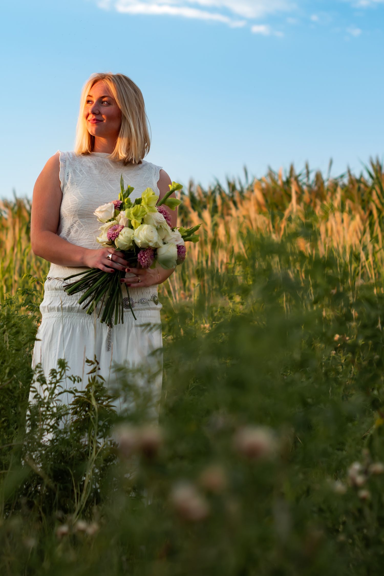 Figure in white dress holding bouquet of flowers in golden sunlit field at sunset.