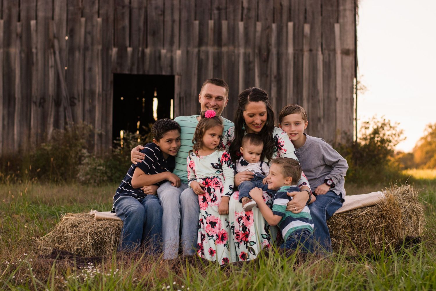 Family relaxing together against a rustic wooden barn wall during sunset.