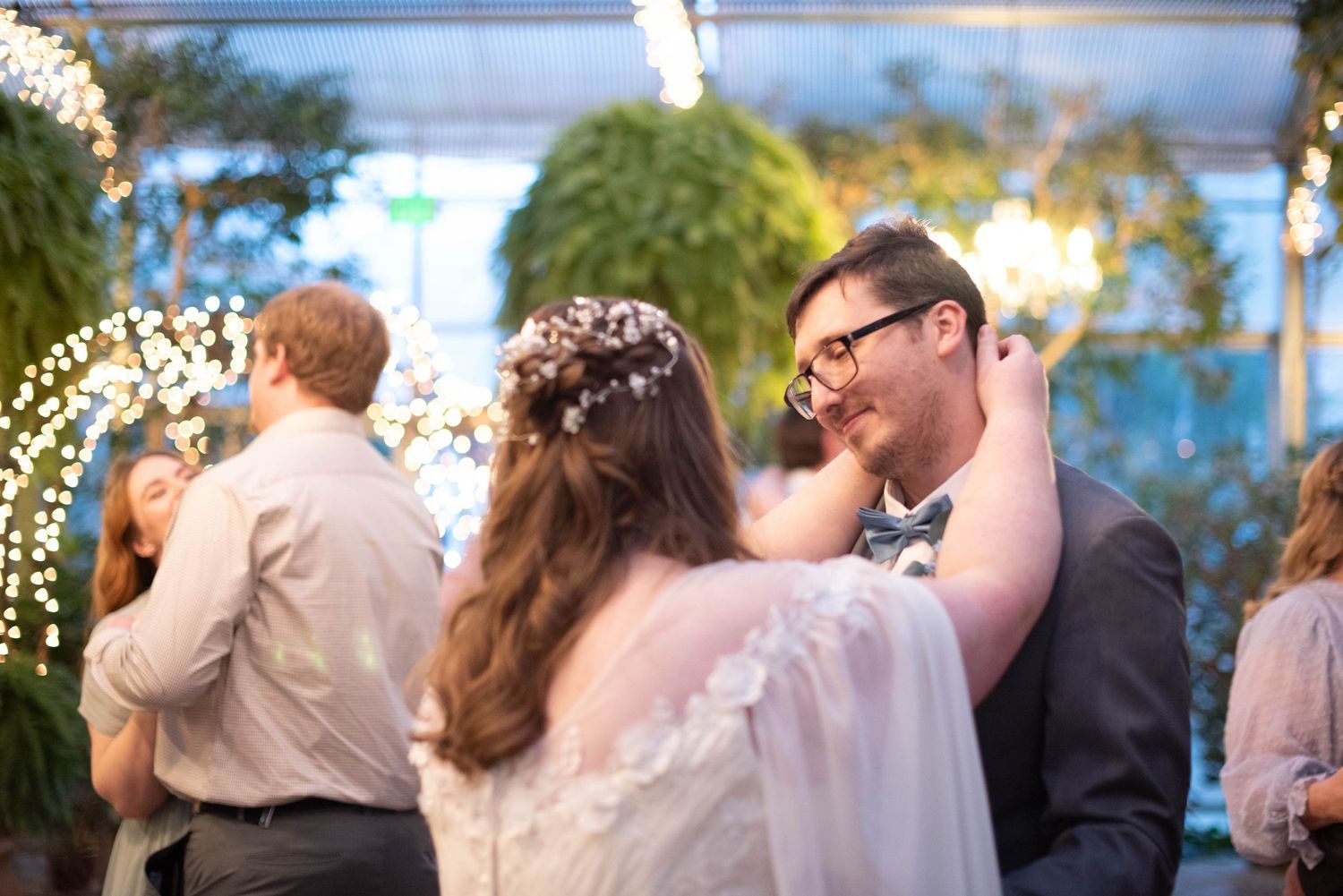 Wedding reception celebration with dancing couples under string lights and greenery.