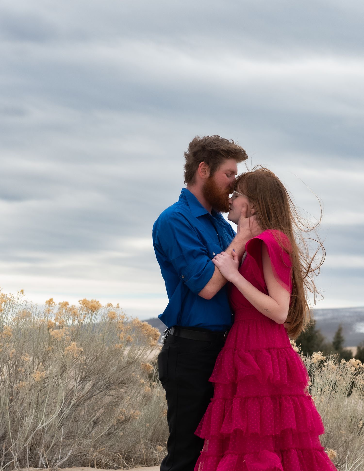 A romantic photoshoot in a field with dramatic cloudy skies and golden grass.