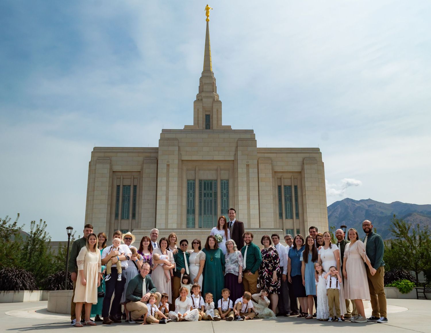 Large group gathered outside a white Mormon temple building with mountains in the background.