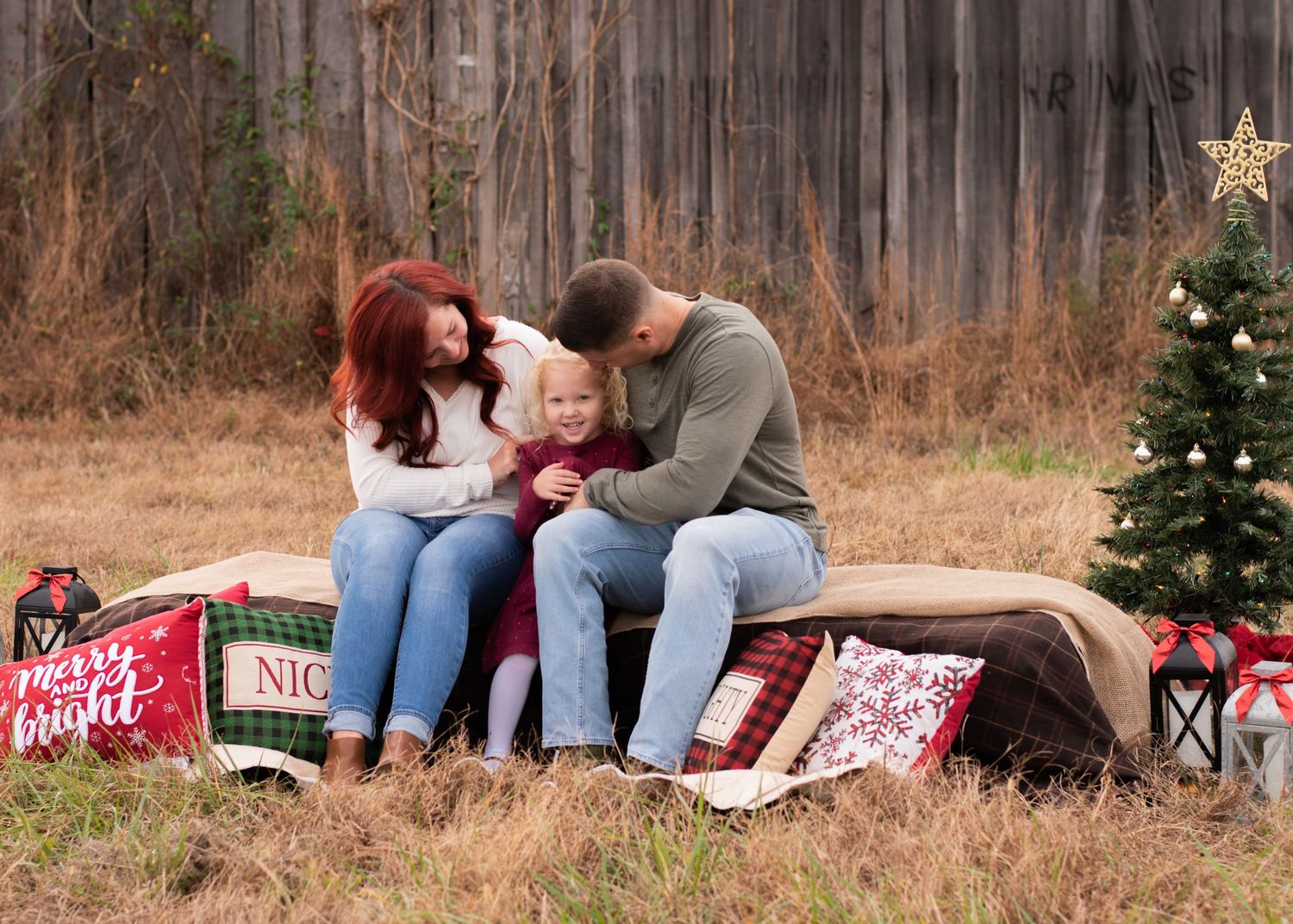 Holiday-themed outdoor photo session with wooden fence and Christmas decorations.
