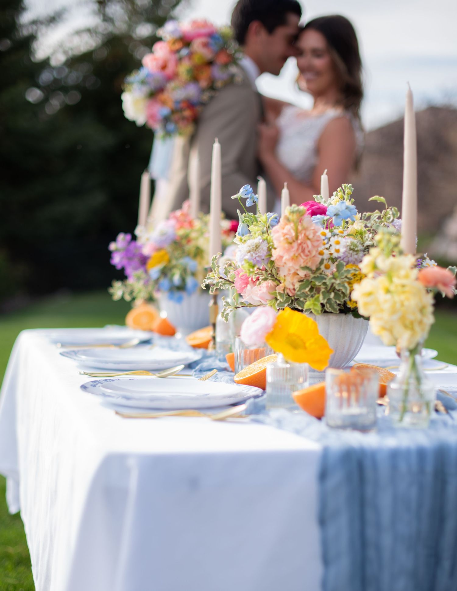 Elegant wedding reception table settings with colorful floral centerpieces and blue linens.