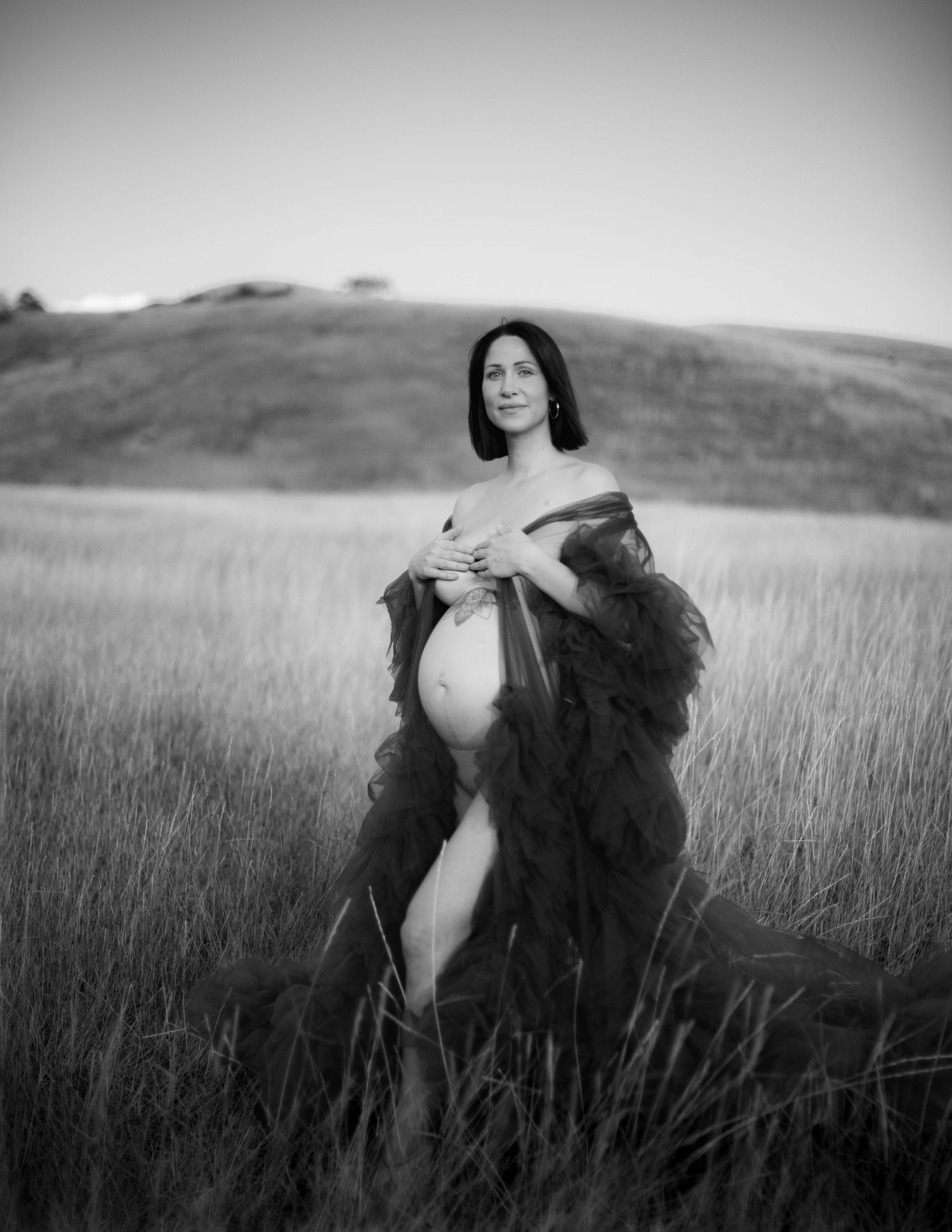 Black and white maternity photos taken in a grassy field with dramatic lighting.