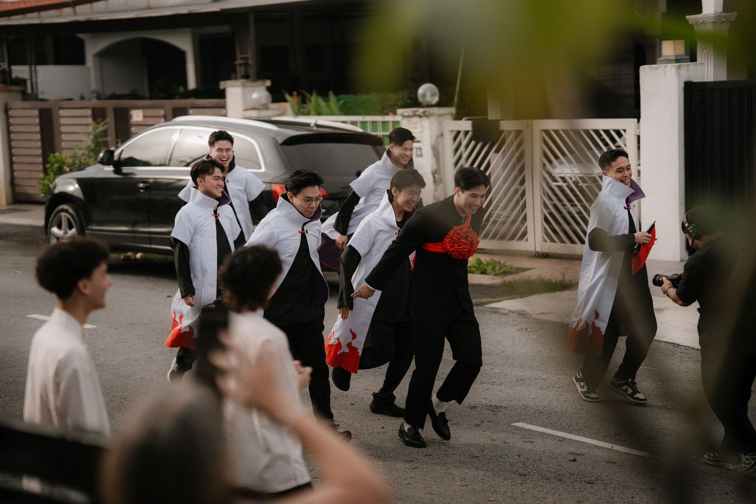 Group of groomsmen in matching light blue shirts and dark trousers walking and laughing together on a street during a wedding procession.