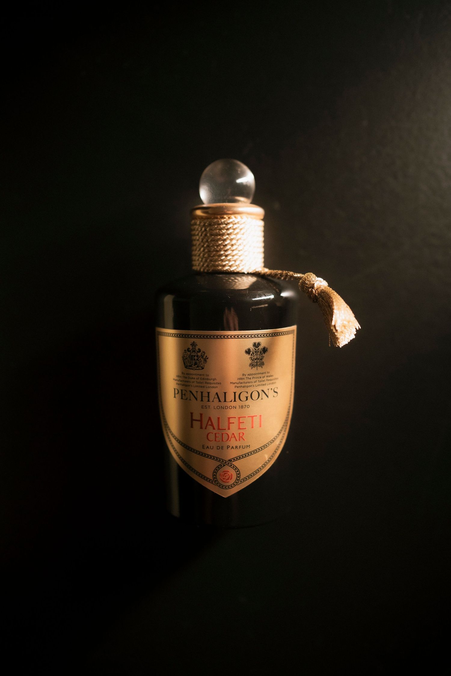 Penhaligon's Halfeti Cedar Eau de Parfum bottle with gold shield label and rope-wrapped neck, glowing against a dark background.