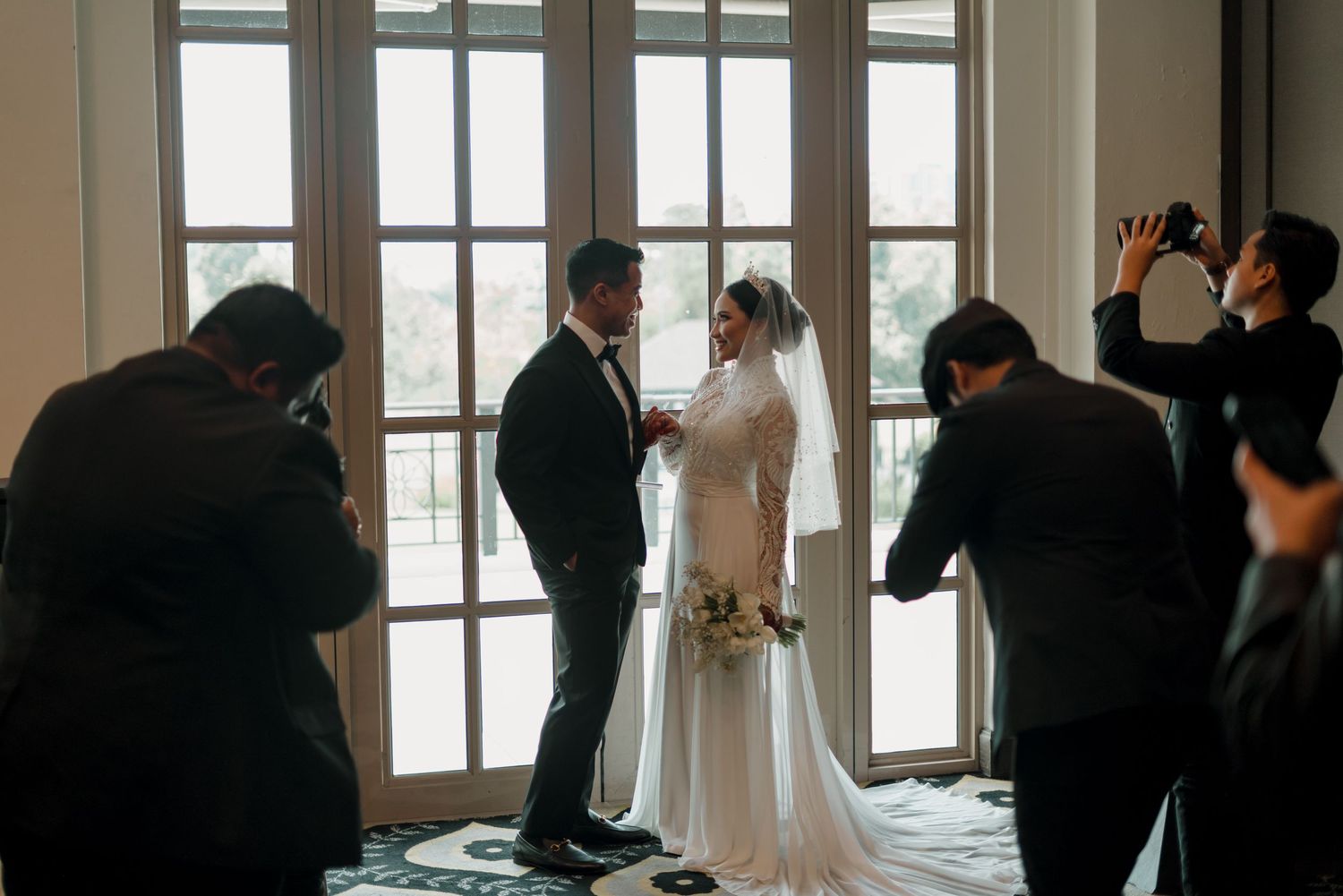 Wedding photographers capture a couple exchanging vows in front of bright French doors during an intimate ceremony.