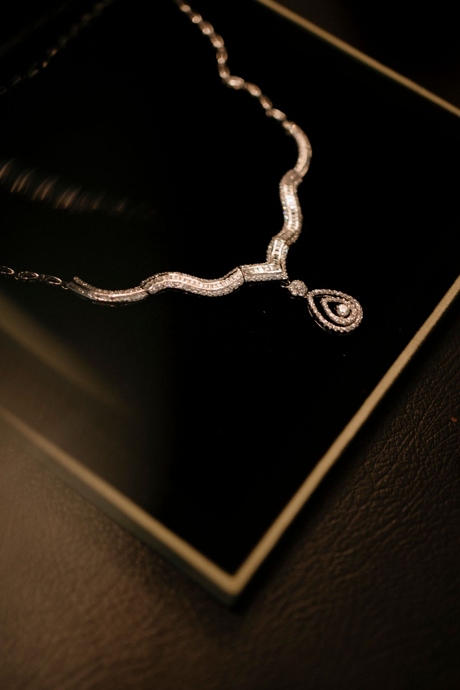 Elegant diamond necklace with a wavy pave setting and teardrop pendant displayed in a black jewelry box.