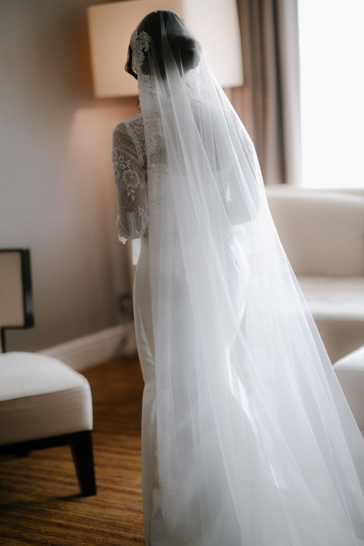 A flowing white wedding veil creates an ethereal effect in soft natural window light.