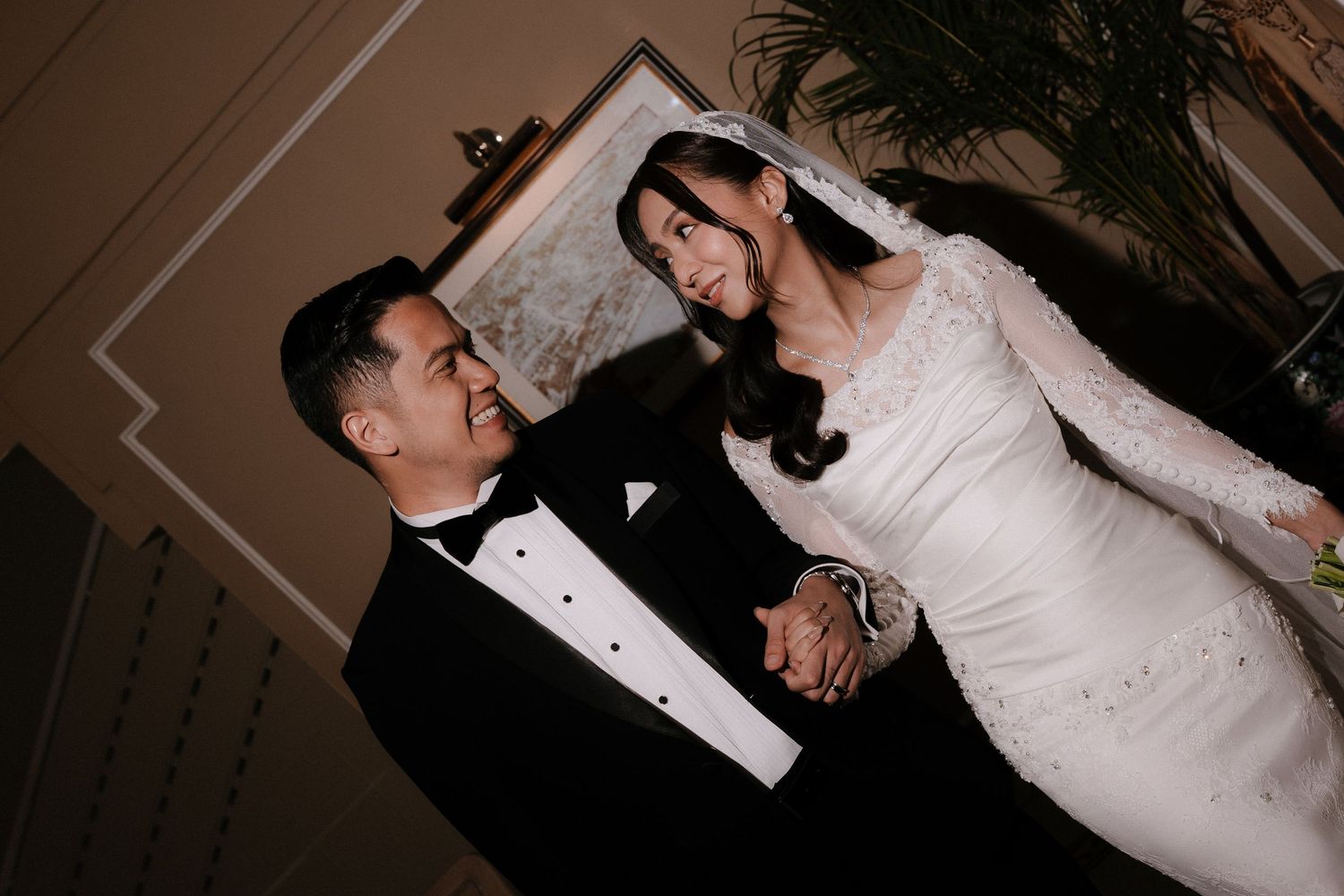 A couple in formal wedding attire dances together during their first dance at a dimly lit reception venue.