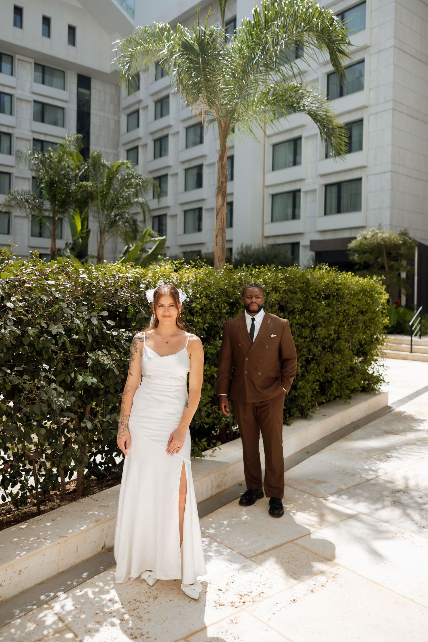 Elegant wedding portrait with modern hotel and palm trees in background.