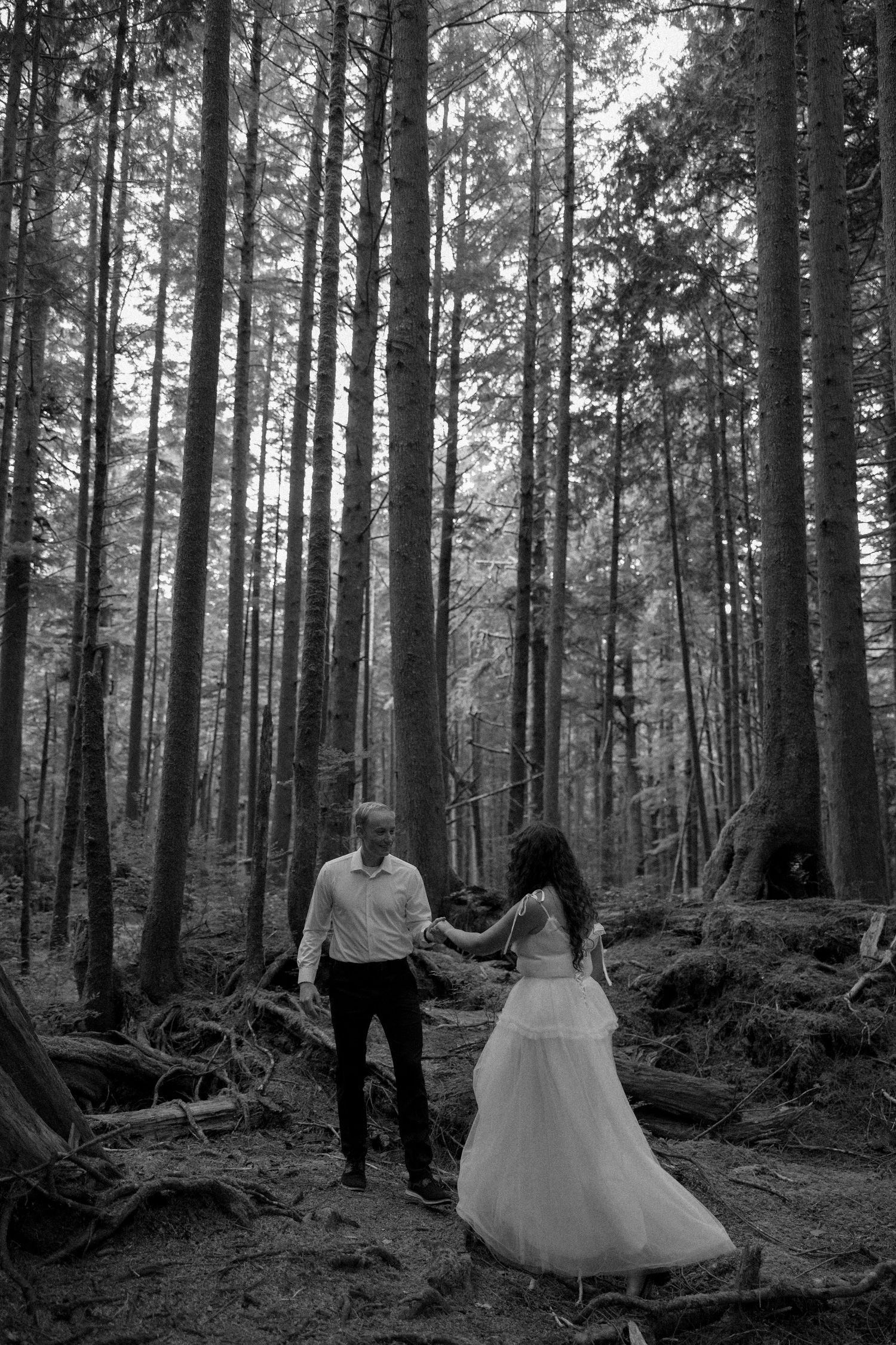A romantic forest wedding photoshoot among tall evergreen trees in black and white.