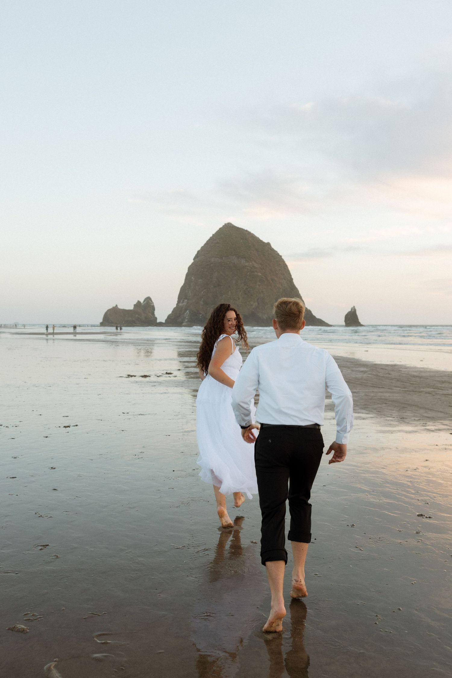 A couple walks barefoot along the shore at Cannon Beach during golden hour.