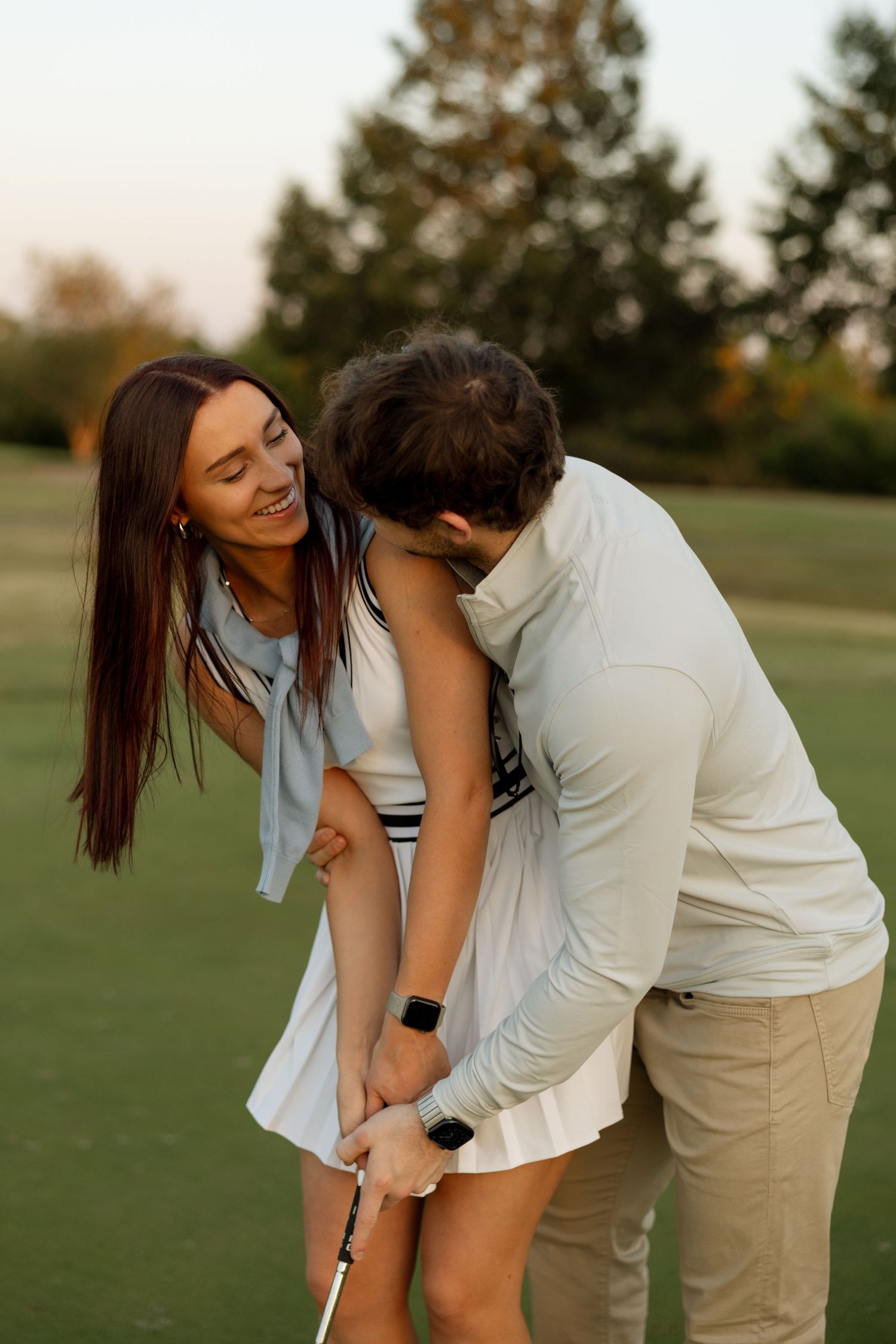 Couple sharing a lighthearted golf lesson moment on the putting green.